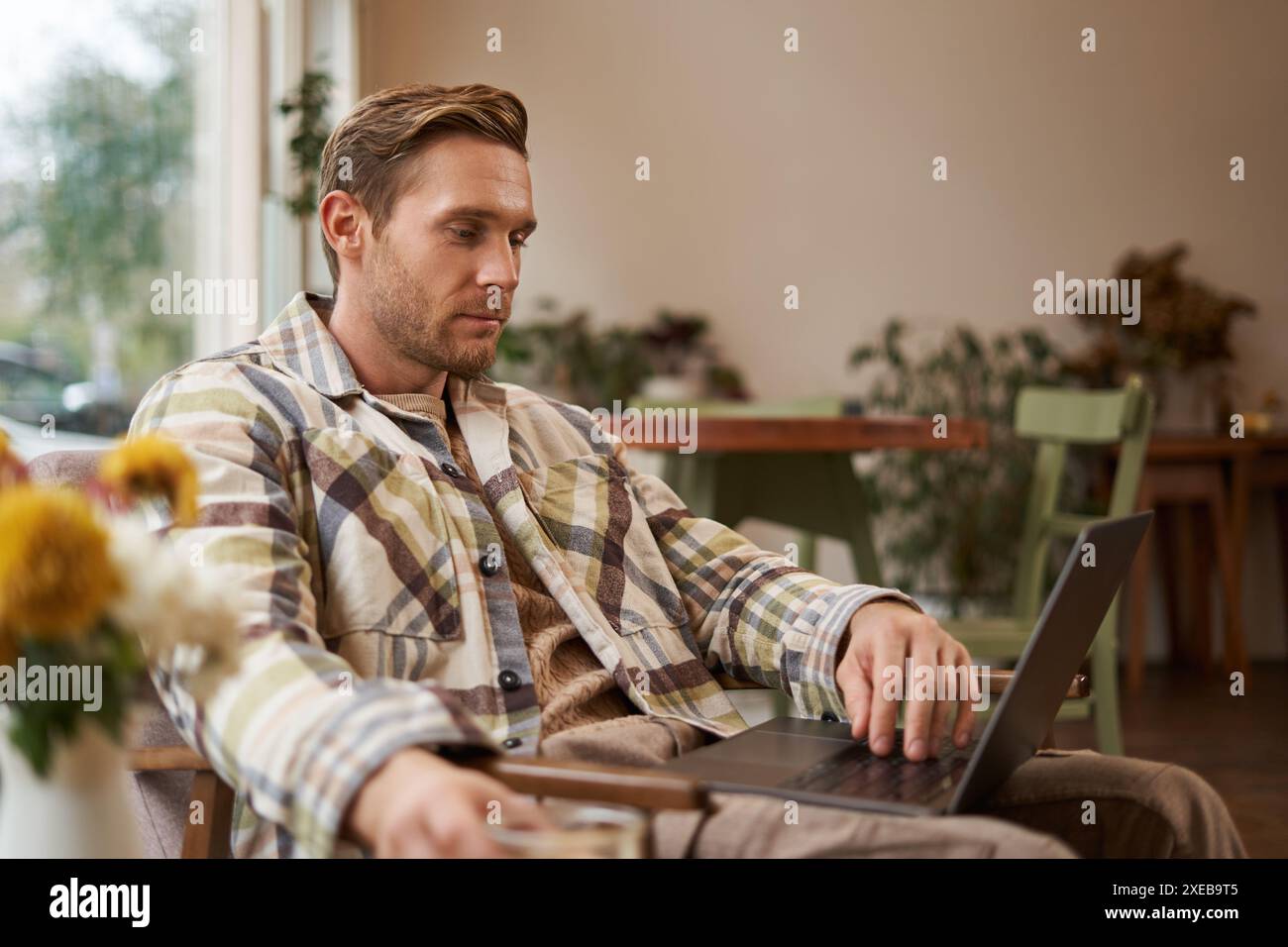 Lifestyle and workplace concept. Young handsome man in casual clothes, sitting in cafe with laptop, studying online, working rem Stock Photo
