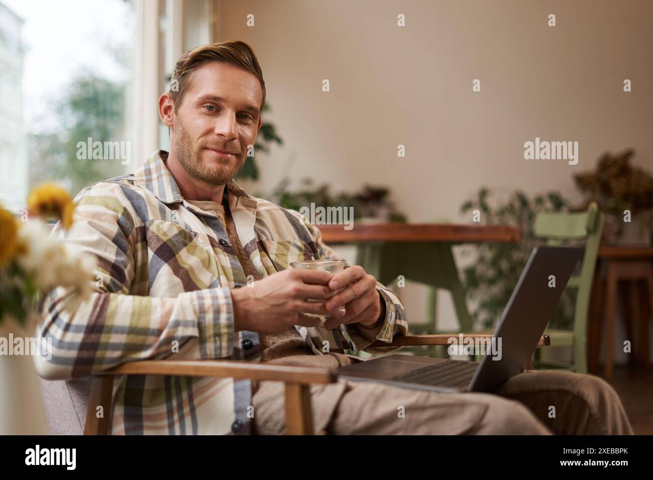 Image of handsome businessman working from cafe, drinking coffee and doing online project on his laptop, smiling and looking hap Stock Photo
