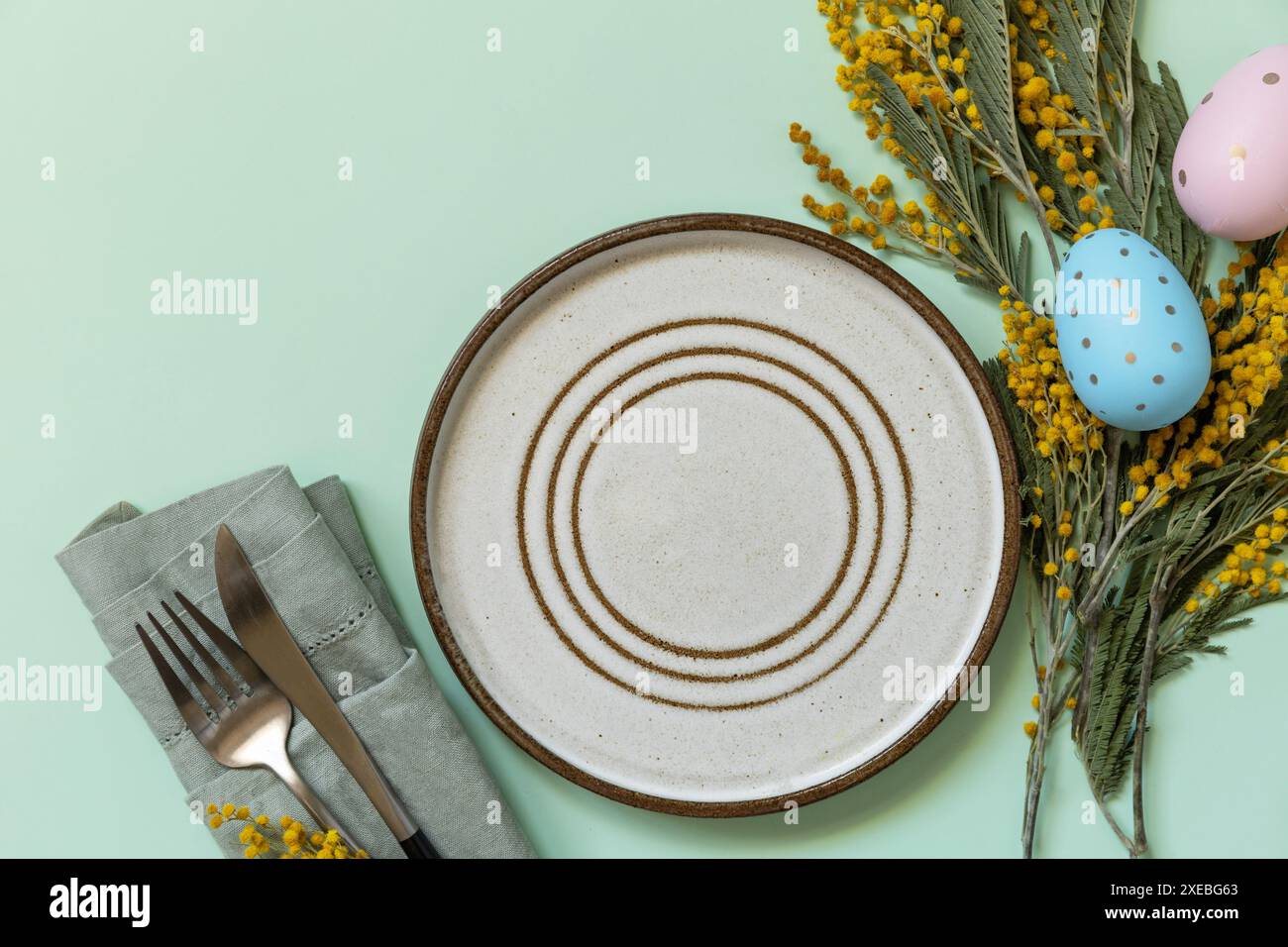 Table setting for Easter dinner with easter eggs and mimosa on a pastel background Stock Photo