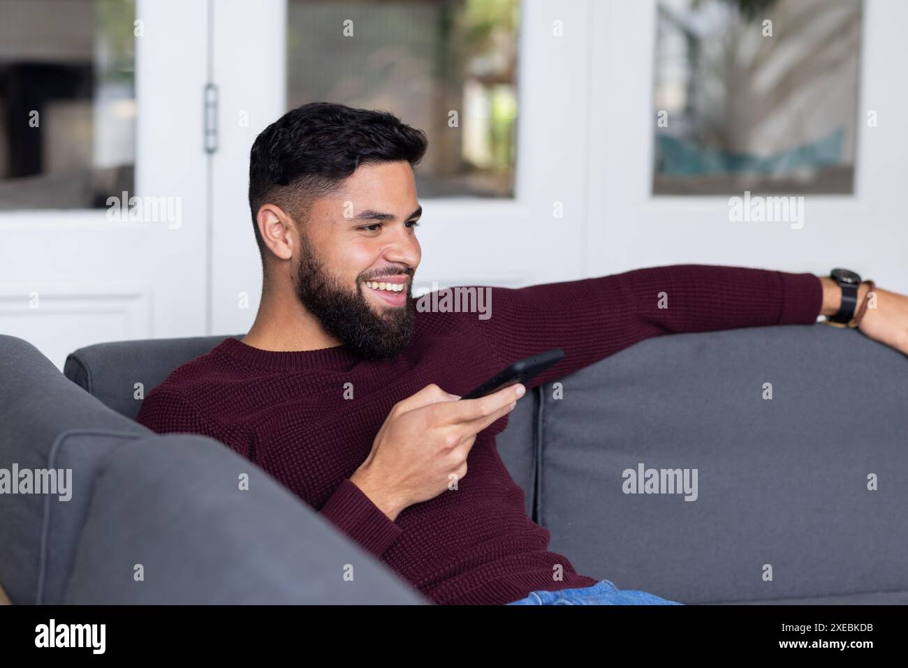 Relaxing on couch, man smiling while using smartphone at home Stock Photo