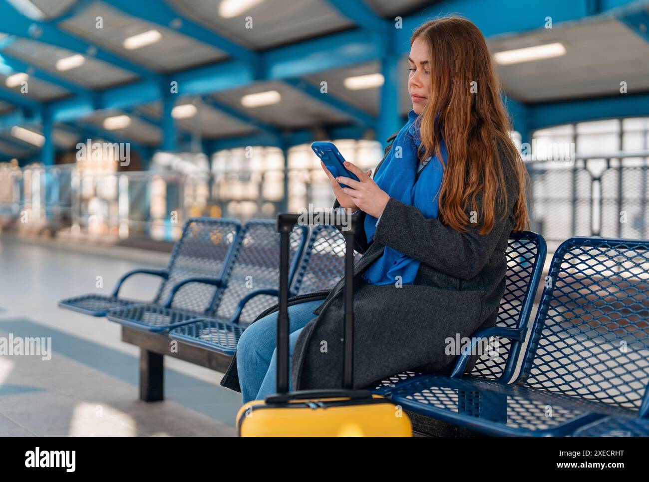 an excited female holding a smartphone while at the train station, airport, bus stop . Safety travel concept Stock Photo