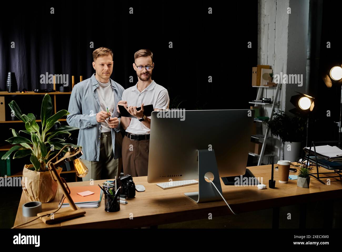Two happy men, stylishly dressed, collaborate on a computer at a desk. Stock Photo