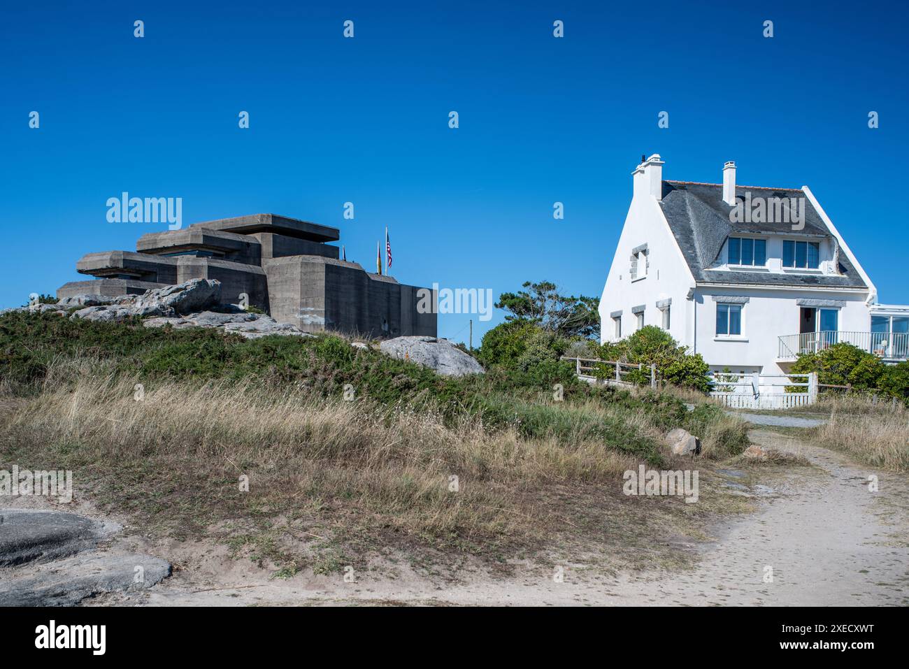 The Grand Bunker of the former German Command and Fire Direction Post in Ouistreham, Brittany, France, alongside a nearby house under a clear blue sky Stock Photo