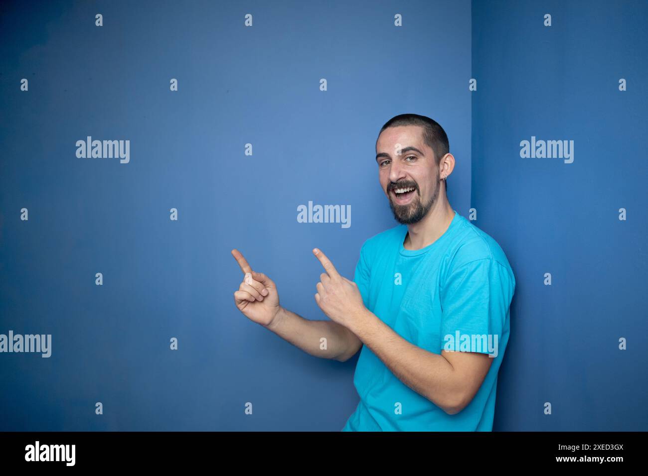 Young man pointing empty space using hands and fingers, isolated over blue background Stock Photo