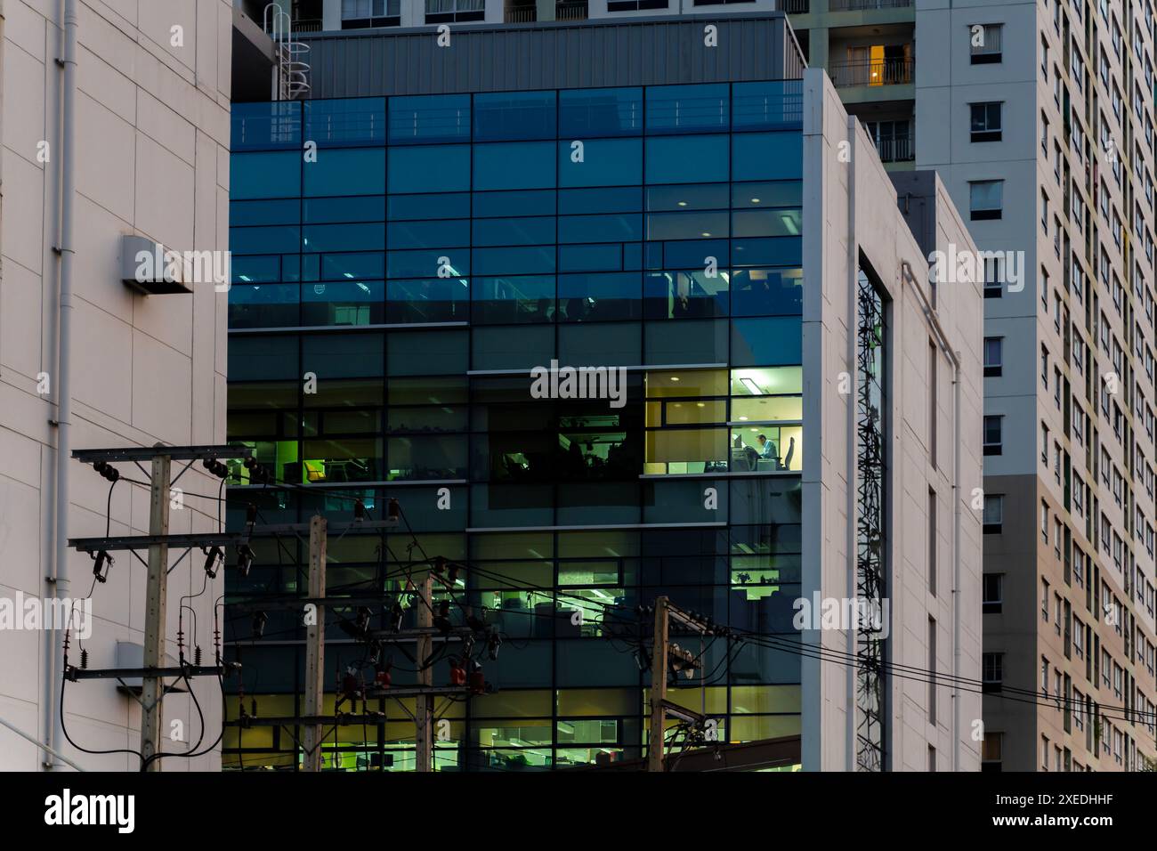 A high-rise building with a glass facade and a power pole in the foreground. A businessperson is standing in an office. The building is located in a c Stock Photo