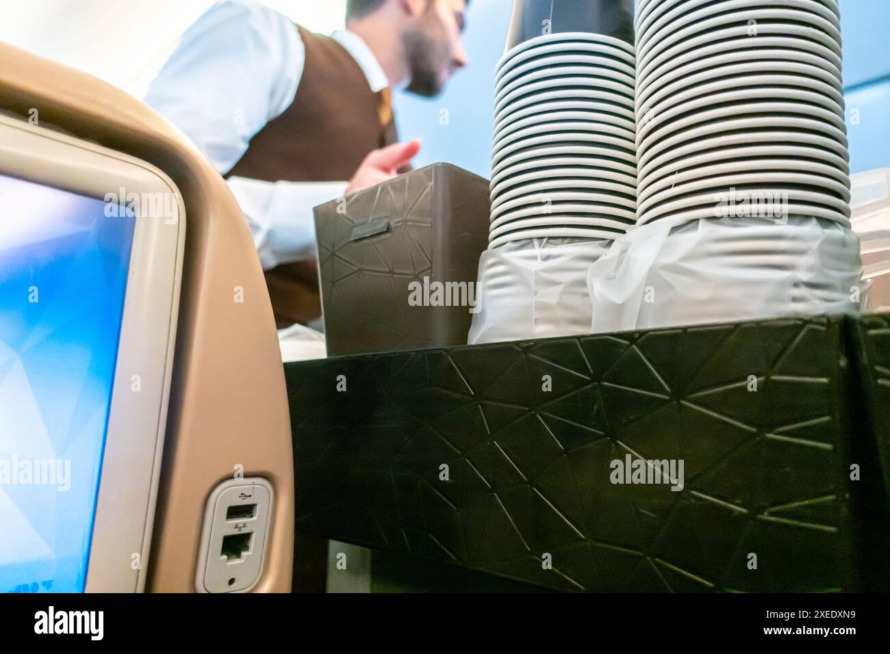Flight attendant serving drinks to passengers sitting in a chair in an airplane cabin Boeing 787-10 Etihad airways Stock Photo
