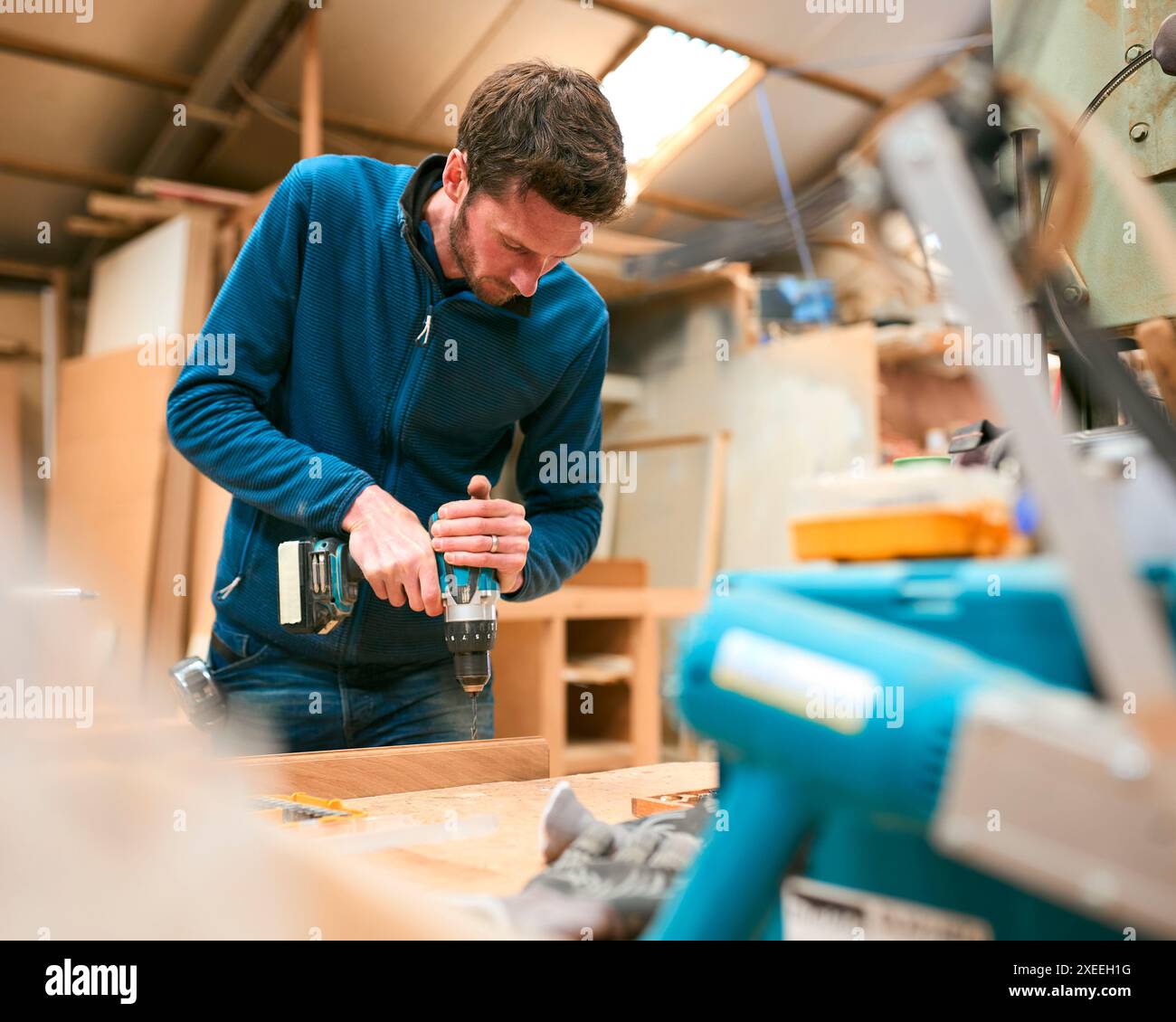 Carpenter At Workbench In Workshop Using Cordless Electric Drill Stock Photo