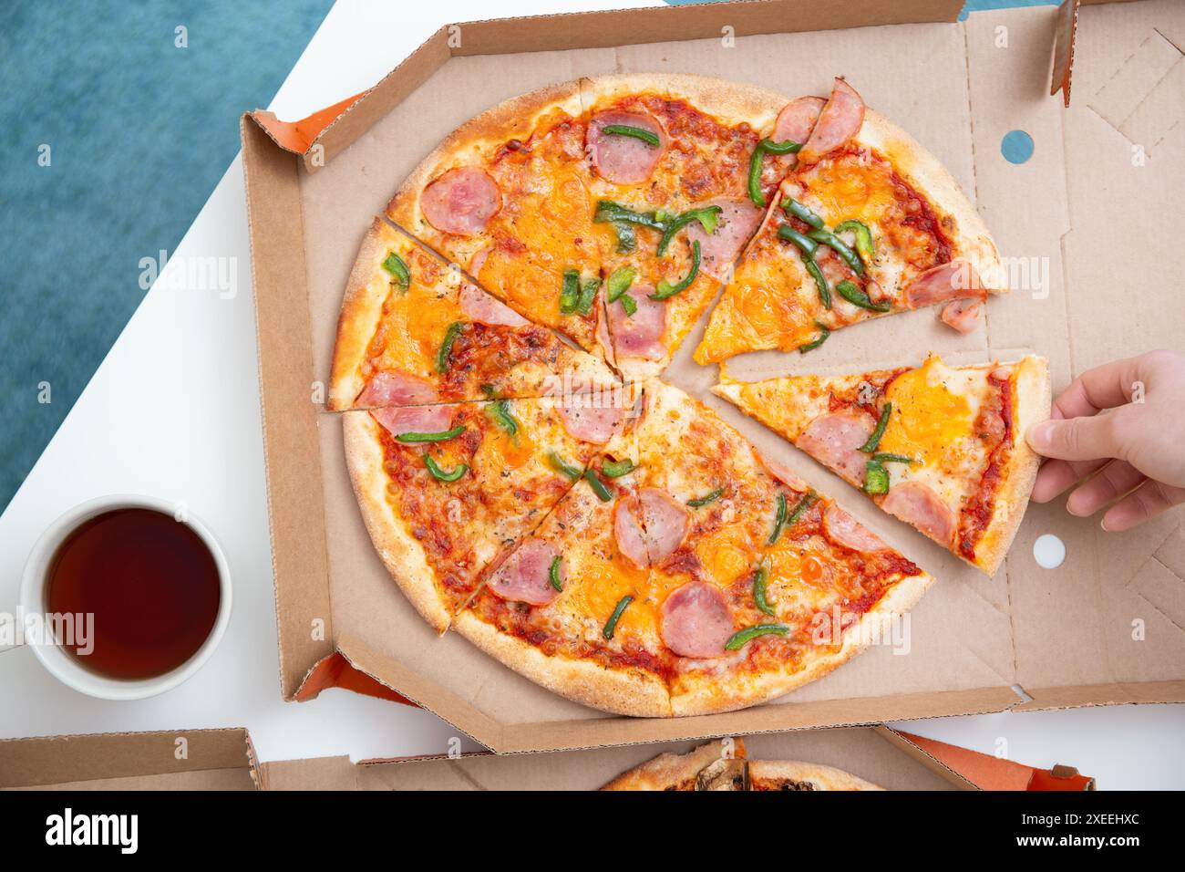 Hand takes a slice of pizza from an open delivery box on a white table, top view Stock Photo
