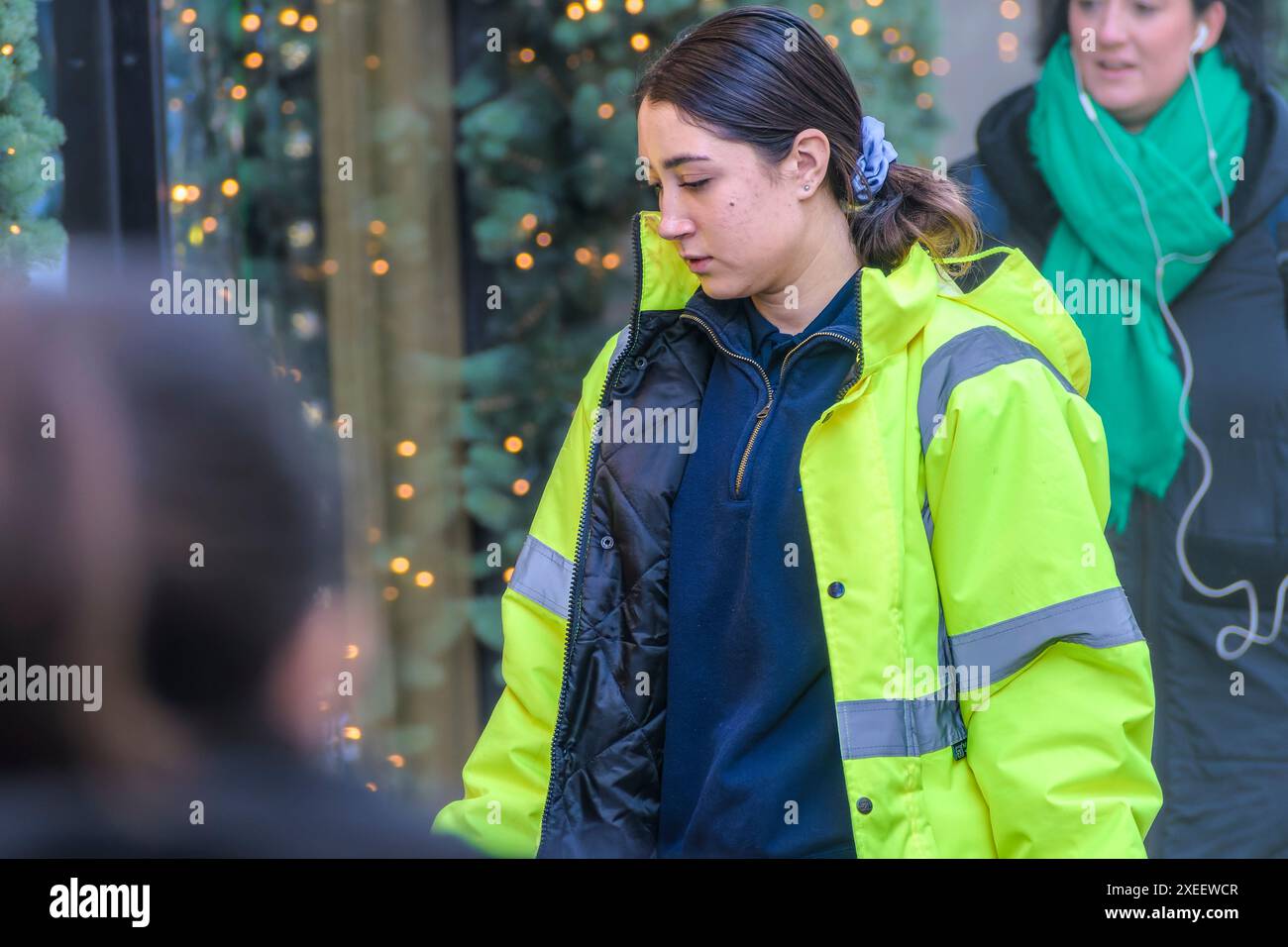 Young woman in working Hi-Viz jacket in front of Christmas decorated shop. Dublin, Ireland. Stock Photo