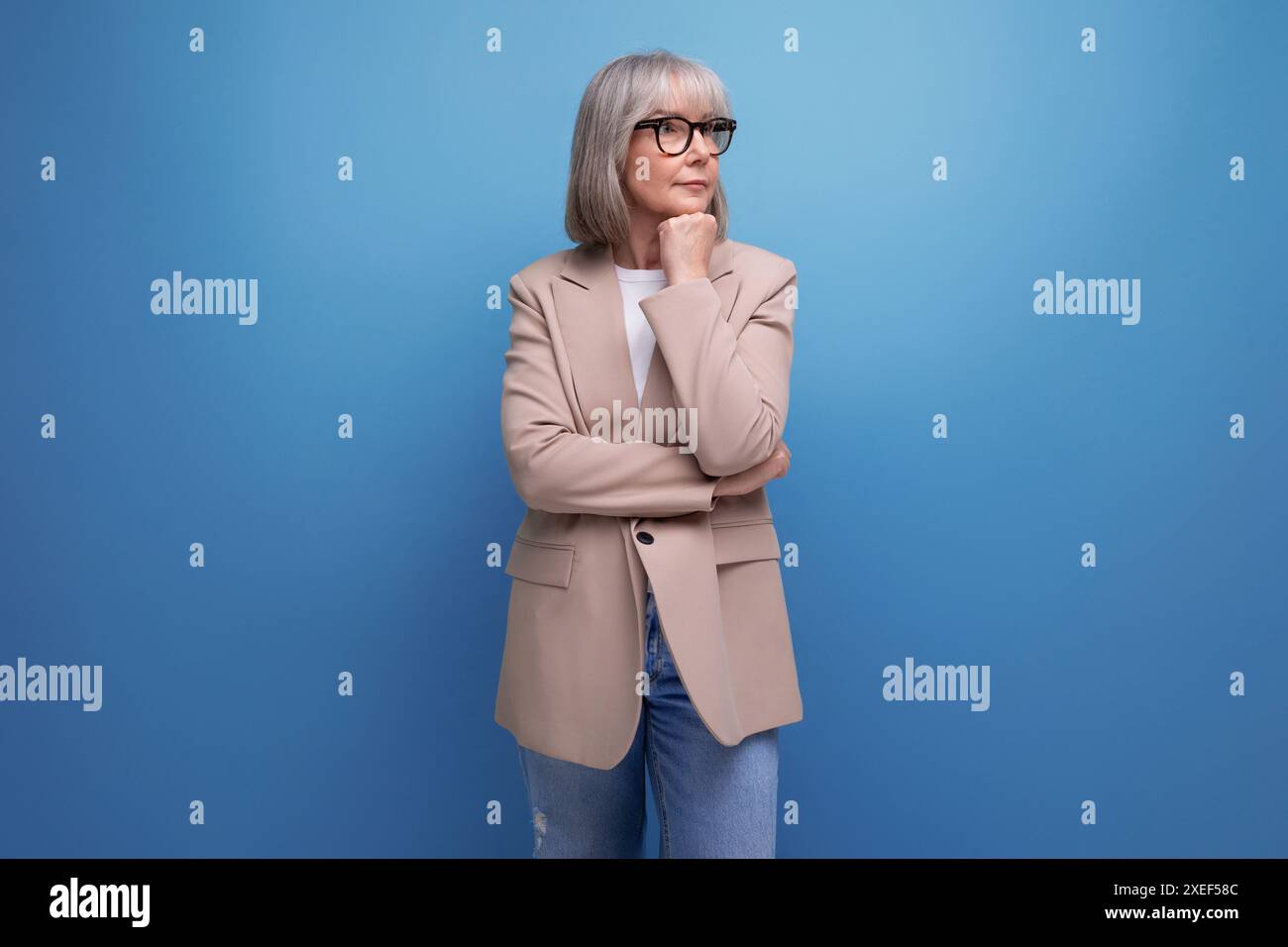 60s mature woman in business attire stands thoughtfully on a studio background with copy space Stock Photo