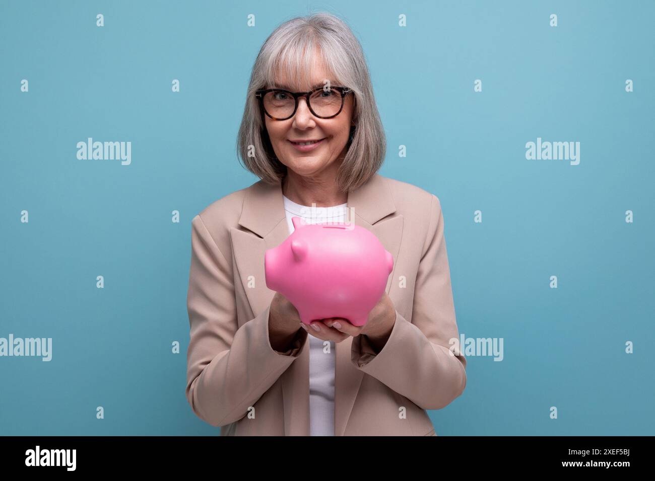 Cute old woman in a jacket with a piggy bank of money savings on a bright background with copy space Stock Photo