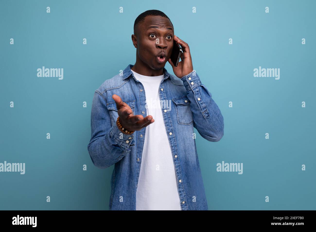 Surprised young american man in denim clothes talking on the phone Stock Photo