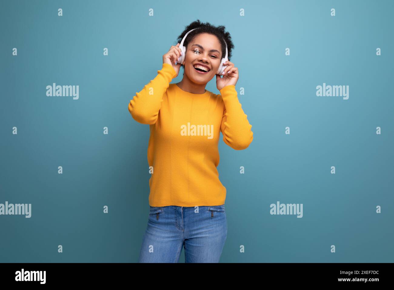 Cheerful young hispanic business woman with black curly hair listening to music in white headphones Stock Photo