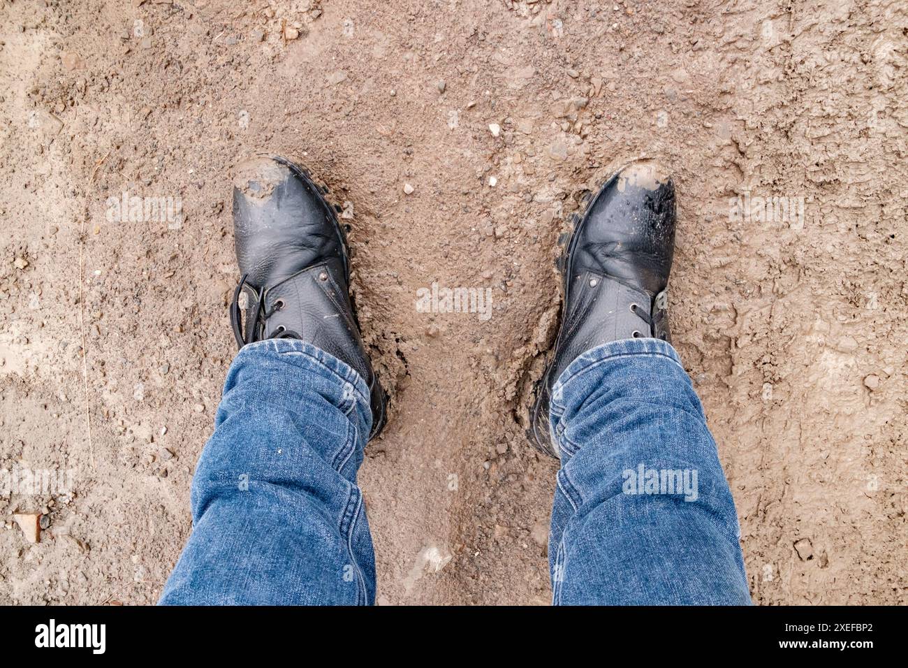 men's feet in jeans and boots standing in the mud, top view Stock Photo