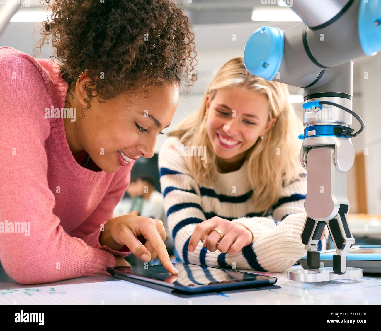Two Female College Or University Engineering Students Using Digital Tablet To Control Robot Arm Stock Photo