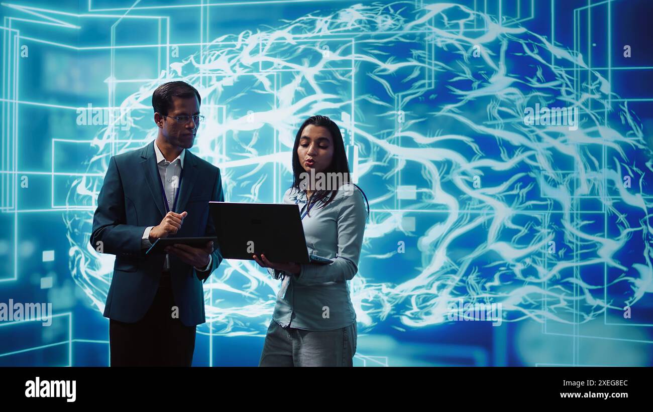 Coworkers solving tasks on laptop and tablet, running artificial intelligence programming scripts. IT staff members using devices to write lines of code for AI applications development, camera B Stock Photo