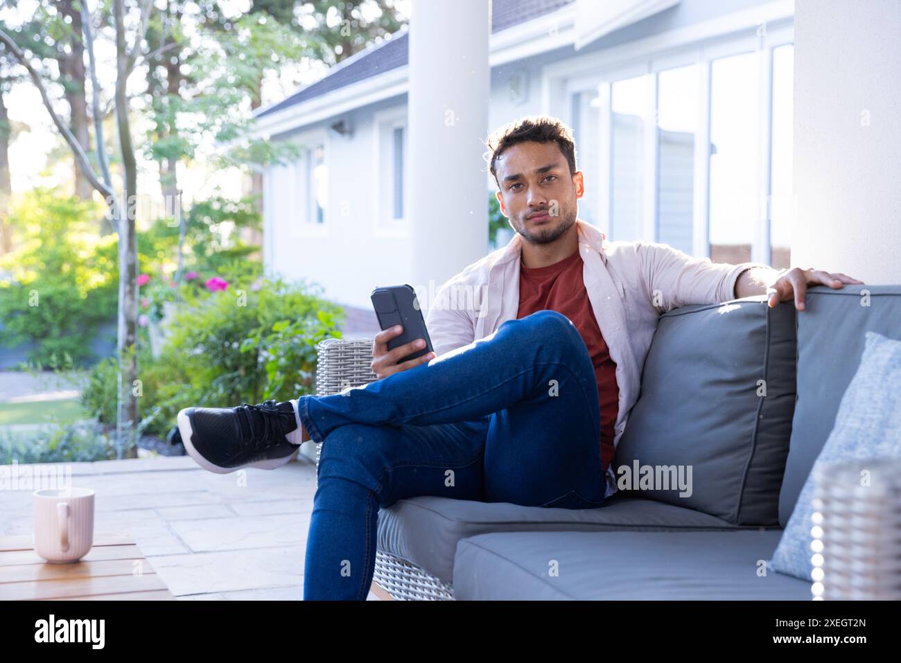 Sitting on outdoor sofa, man holding smartphone and relaxing at home Stock Photo