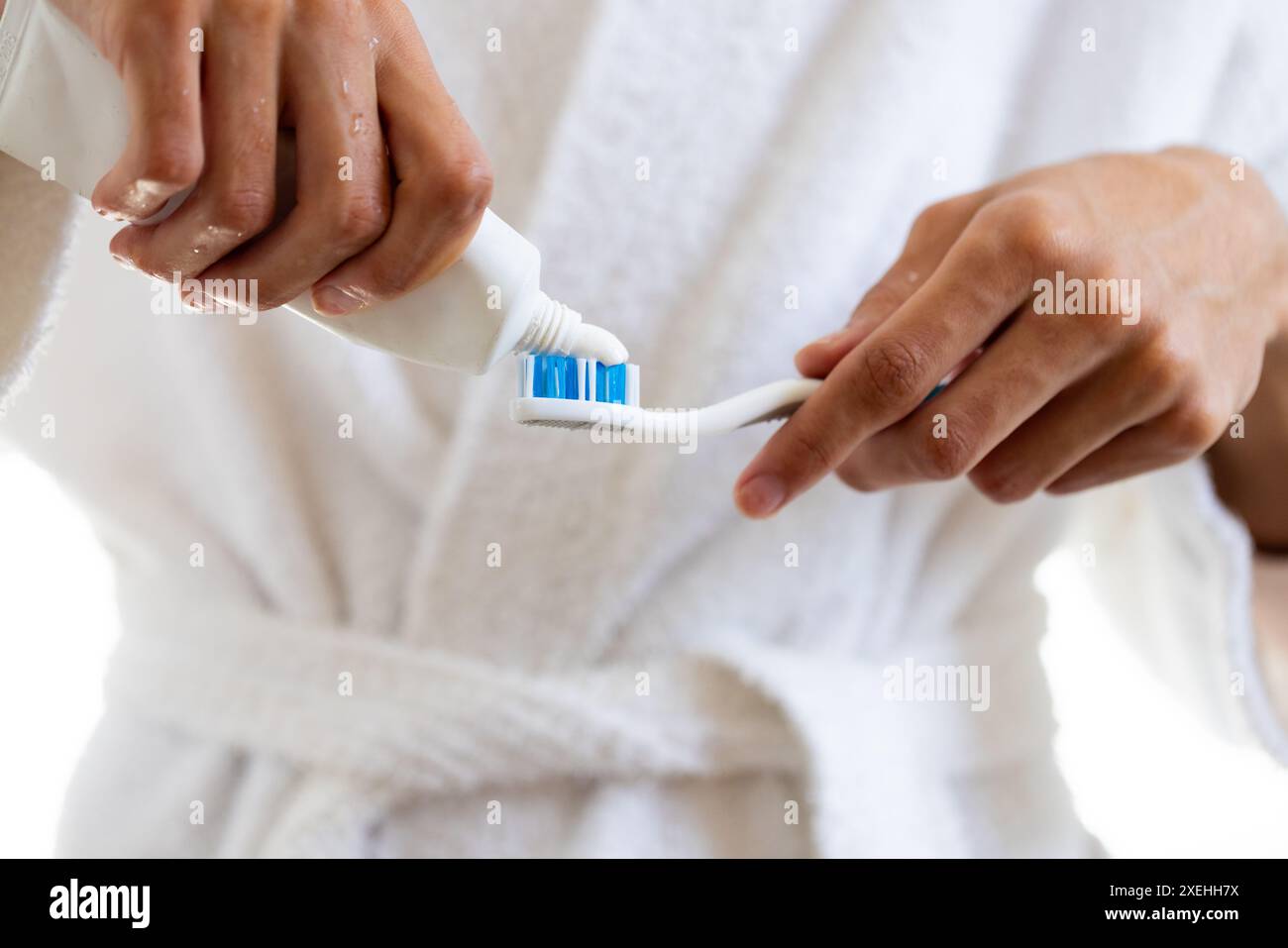 Applying toothpaste on toothbrush, young man in bathrobe preparing for ...
