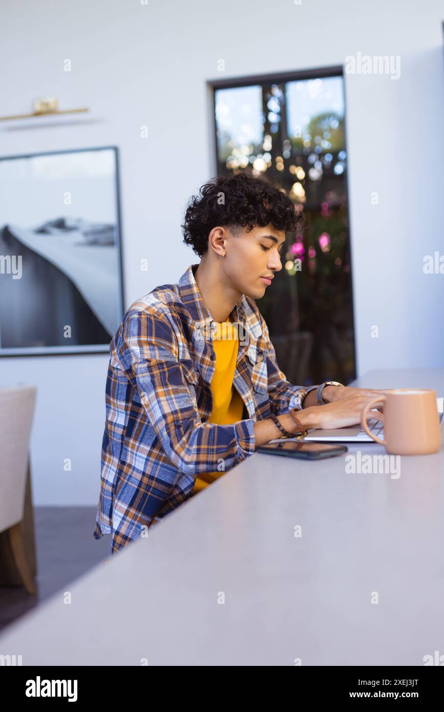 Writing in notebook, teenage boy sitting at table with smartphone and mug Stock Photo