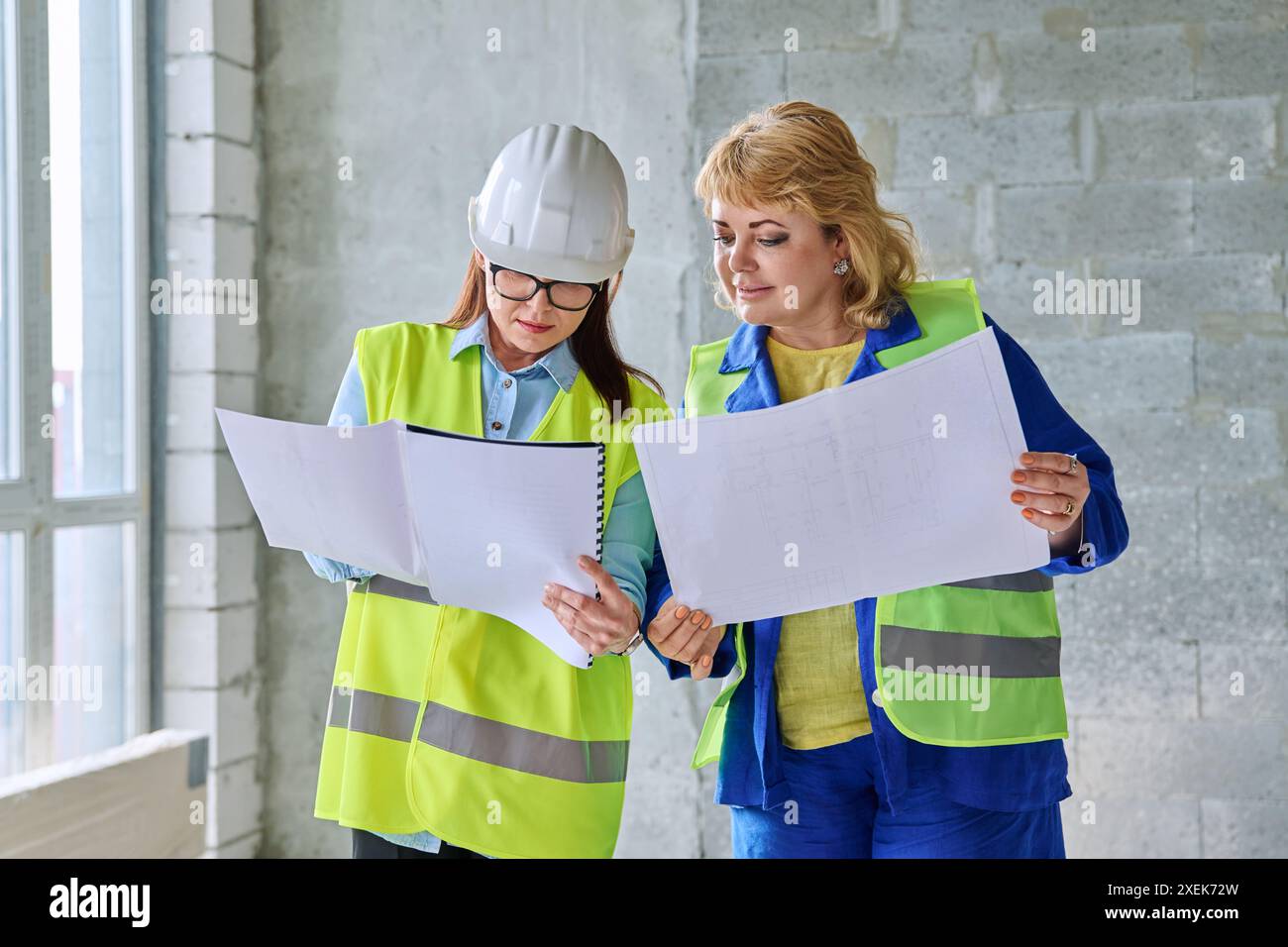 Two female industrial workers with technical plan at construction site Stock Photo