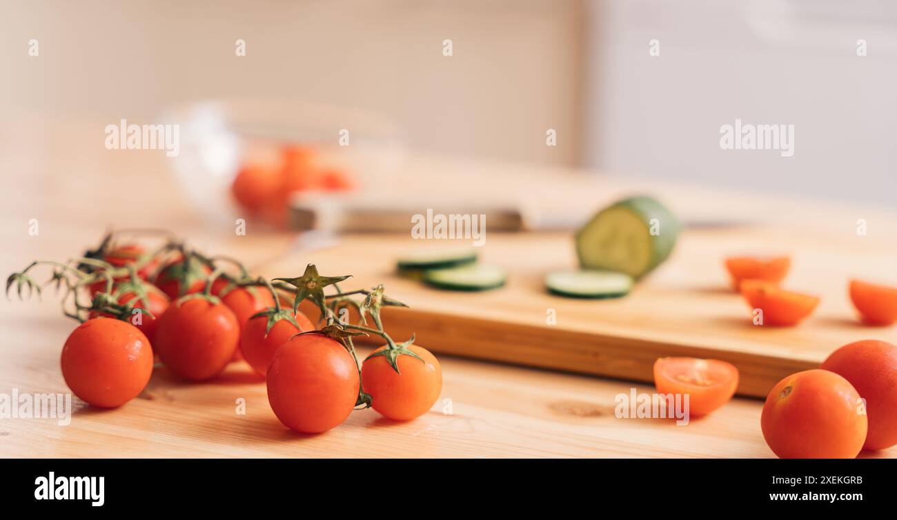 Slicing cherry tomatoes and cucumbers on a wooden cutting board Stock Photo