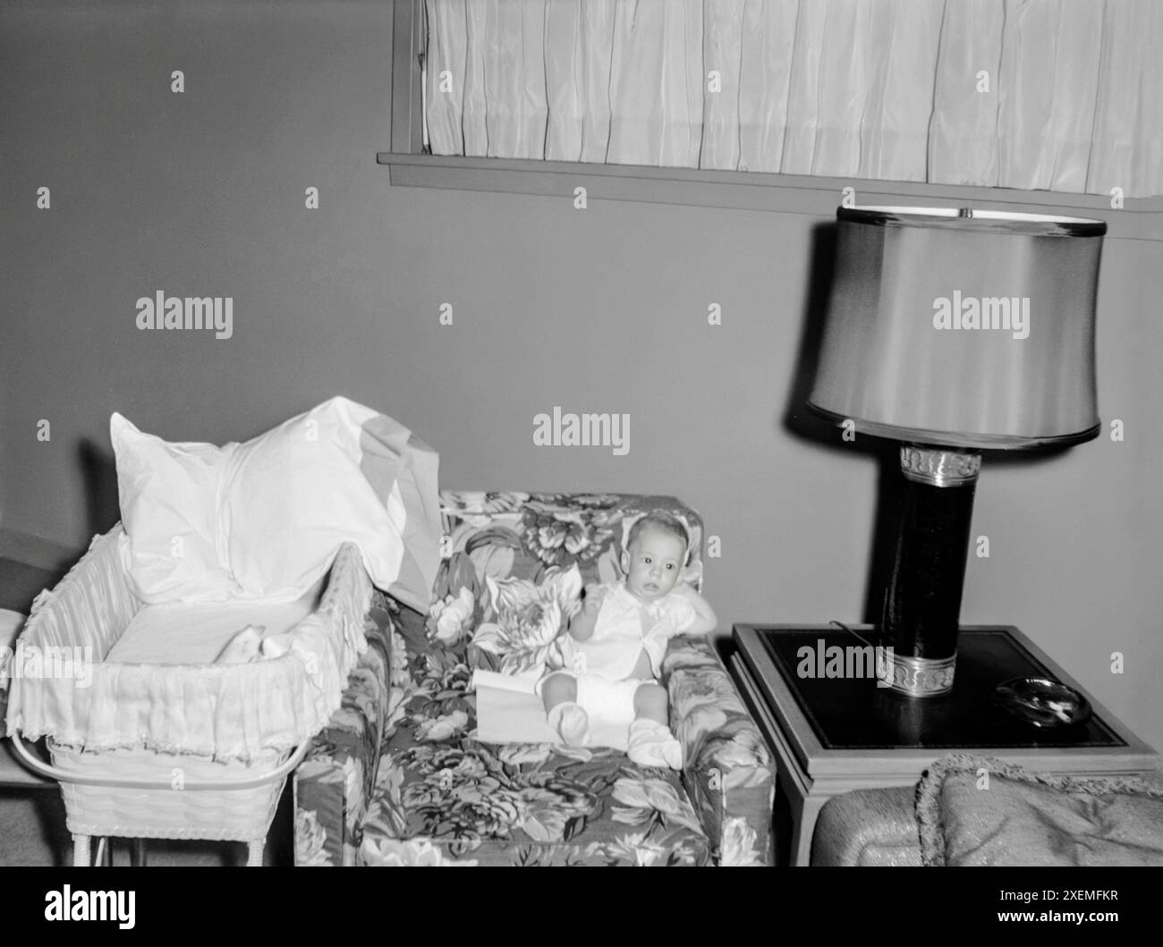 Horizontal shot of a baby boy sitting in a chair next to his bassinet. Stock Photo