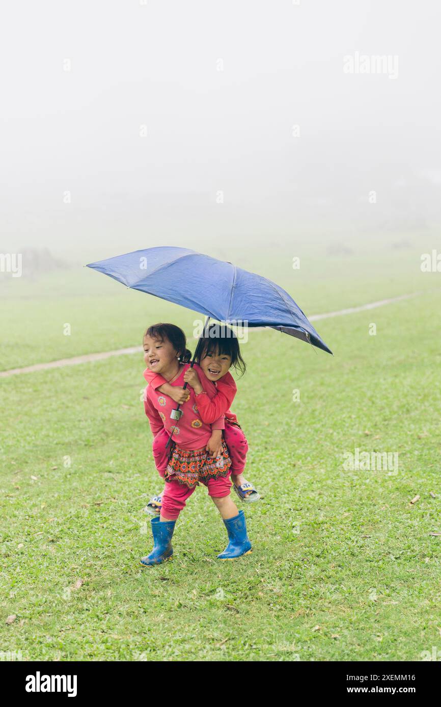 Two girls with an umbrella being silly on a rainy day; Ta So village, Moc Chau District, Son La, Vietnam Stock Photo