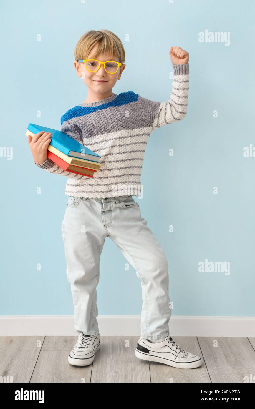Cute little boy with books standing against color wall Stock Photo - Alamy