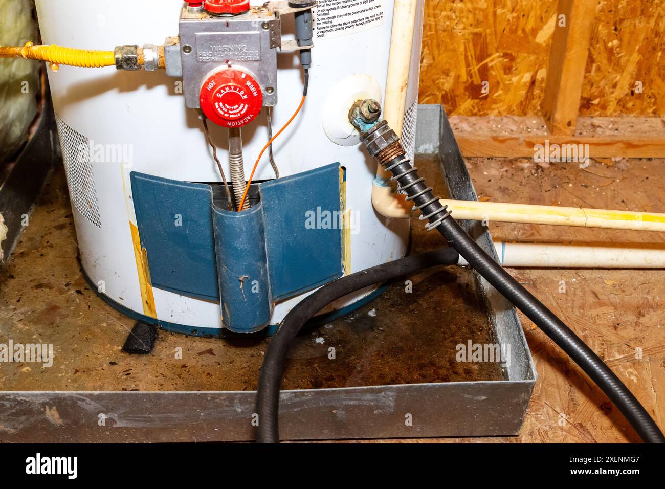 Hose connected to water heater drain, water in catch pan Stock Photo