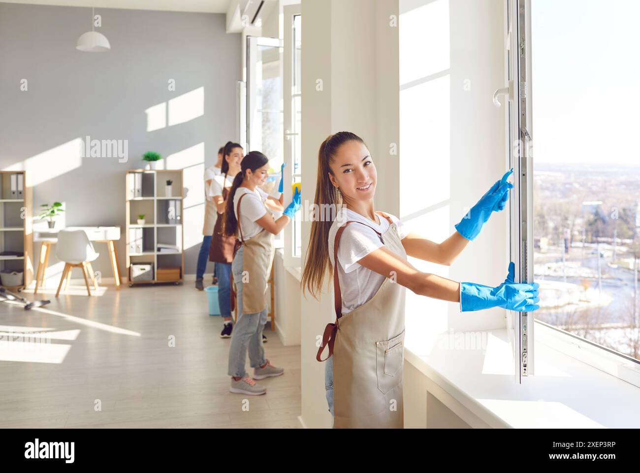 Team of a young janitors cleaning windows in office or at home and looking cheerful at camera. Stock Photo