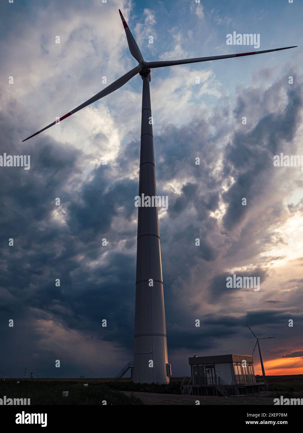 Bottom view of a tall wind turbine silhouette against dramatic sunset ...