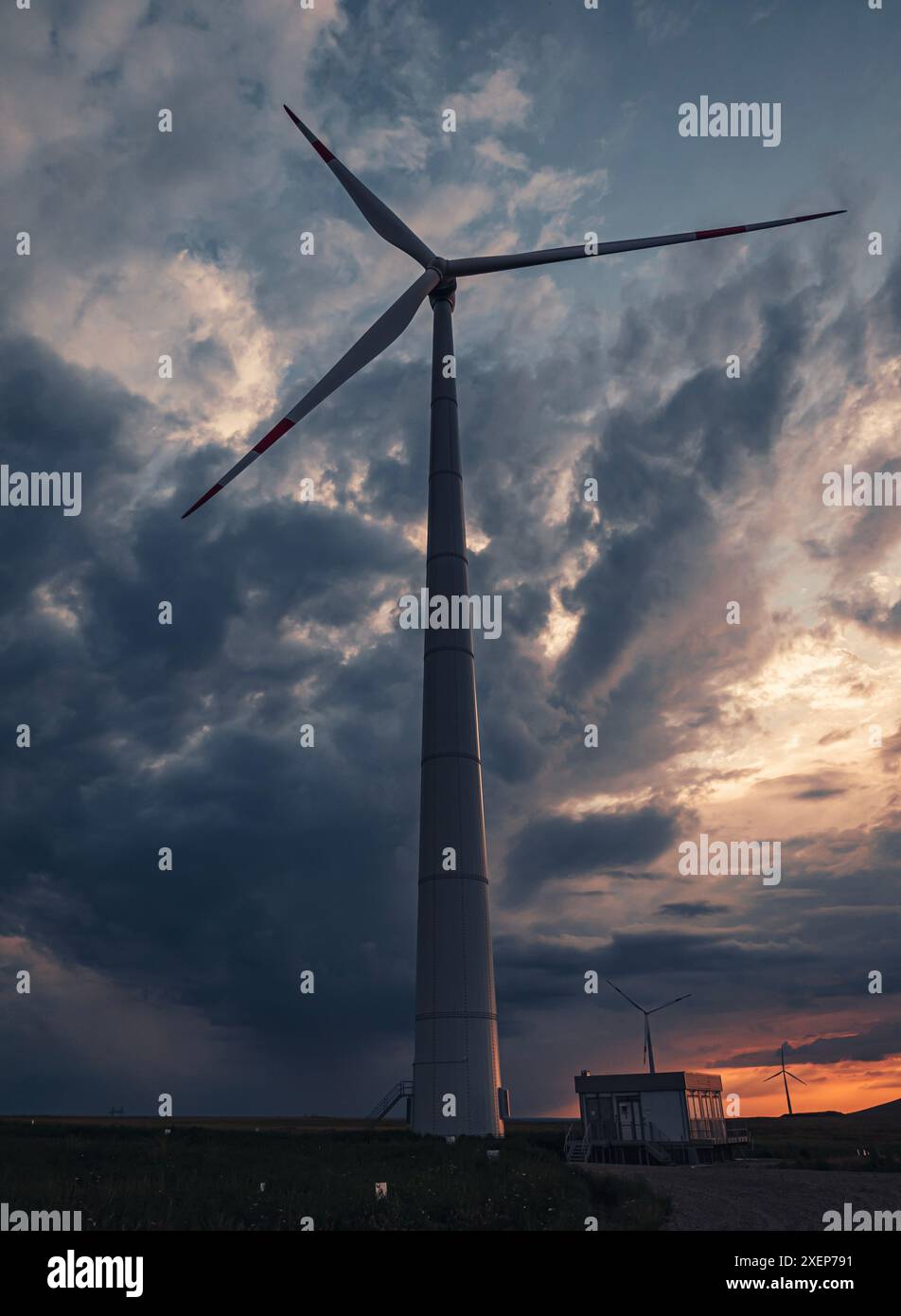 Bottom view of a tall wind turbine silhouette against dramatic sunset ...