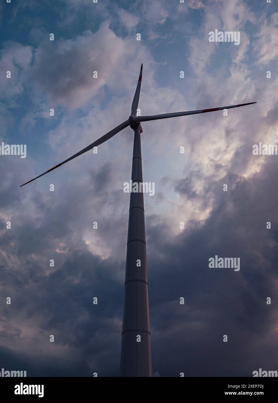 Bottom view of a tall wind turbine silhouette against dramatic sunset ...