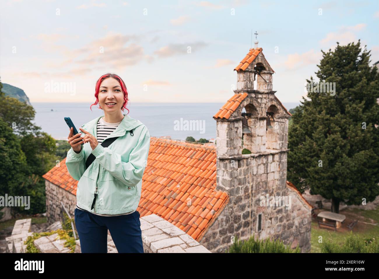 A young woman tourist exploring a monastery in Montenegro, using a smartphone app for navigation. Stock Photo