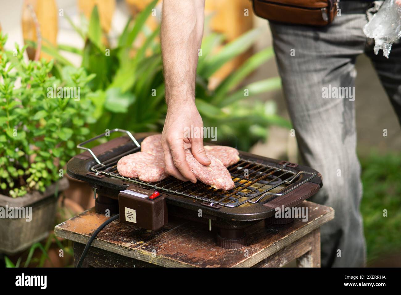 A man putting raw burgers on a barbecue grill Stock Photo