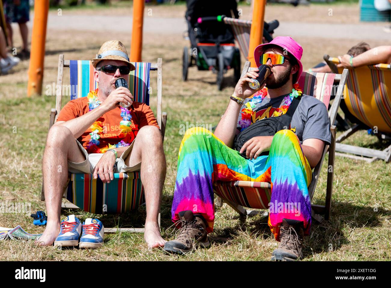 Glastonbury, UK. Day 4, 29 June 2024.  Festival goers in colourful fancy dress sit in deckchairs at Glastonbury Festival, Worthy Farm in Somerset. Picture date: Saturday June 29, 2024. Photo credit should read: David Jensen / Alamy Live News Stock Photo