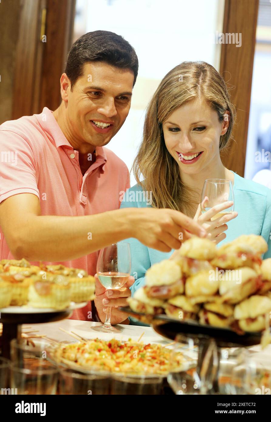 Couple drinking wine and eating tapas. Pintxos. Bar txondorra. Parte Vieja. Old town. San Sebastian. Donostia. Gipuzkoa. Basque Country. Spain. Stock Photo