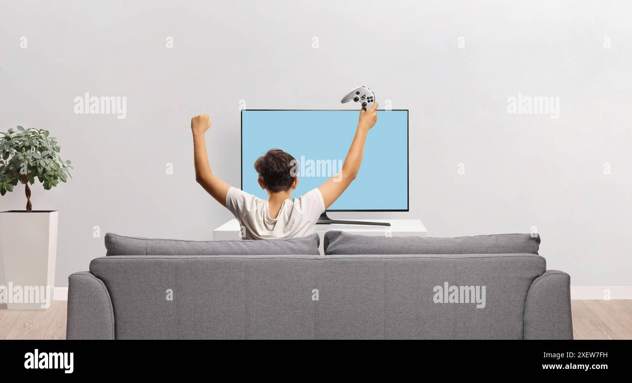 Rear view shot of a happy kid sitting on a sofa with a joystick and ...