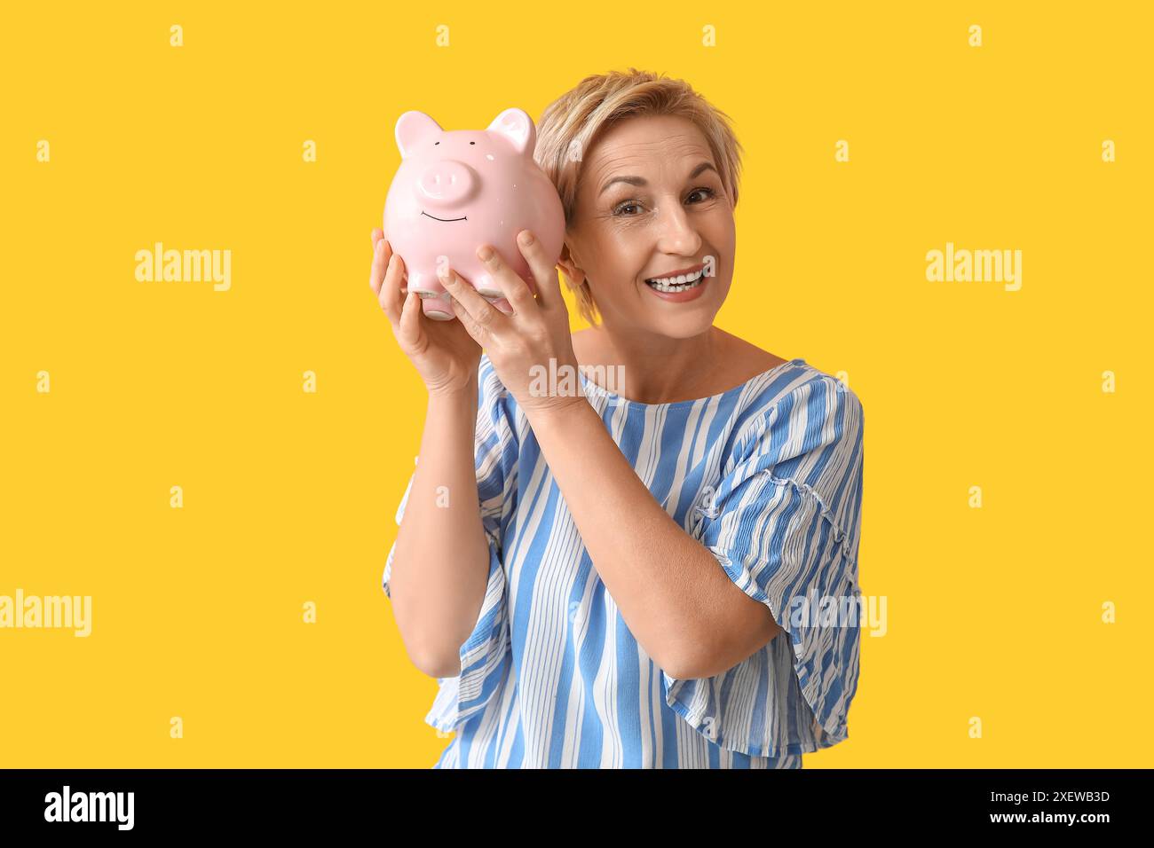 Beautiful mature woman with pink piggy bank on yellow background Stock ...