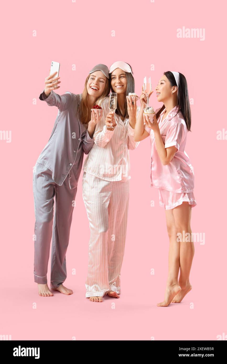 Young women in pajamas with cupcakes and champagne taking selfie on ...