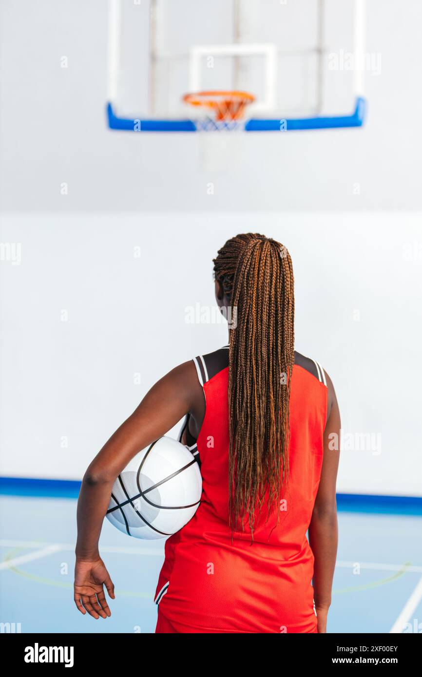 Photo a female basketball player in a red uniform stands on an indoor court, holding a basketball and focusing on the hoop, ready to make a shot. Her Stock Photo