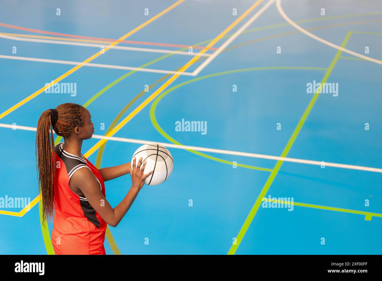 Horizontal photo a female basketball player in a red uniform stands on a vibrant indoor court, holding a basketball and preparing to make a pass, demo Stock Photo