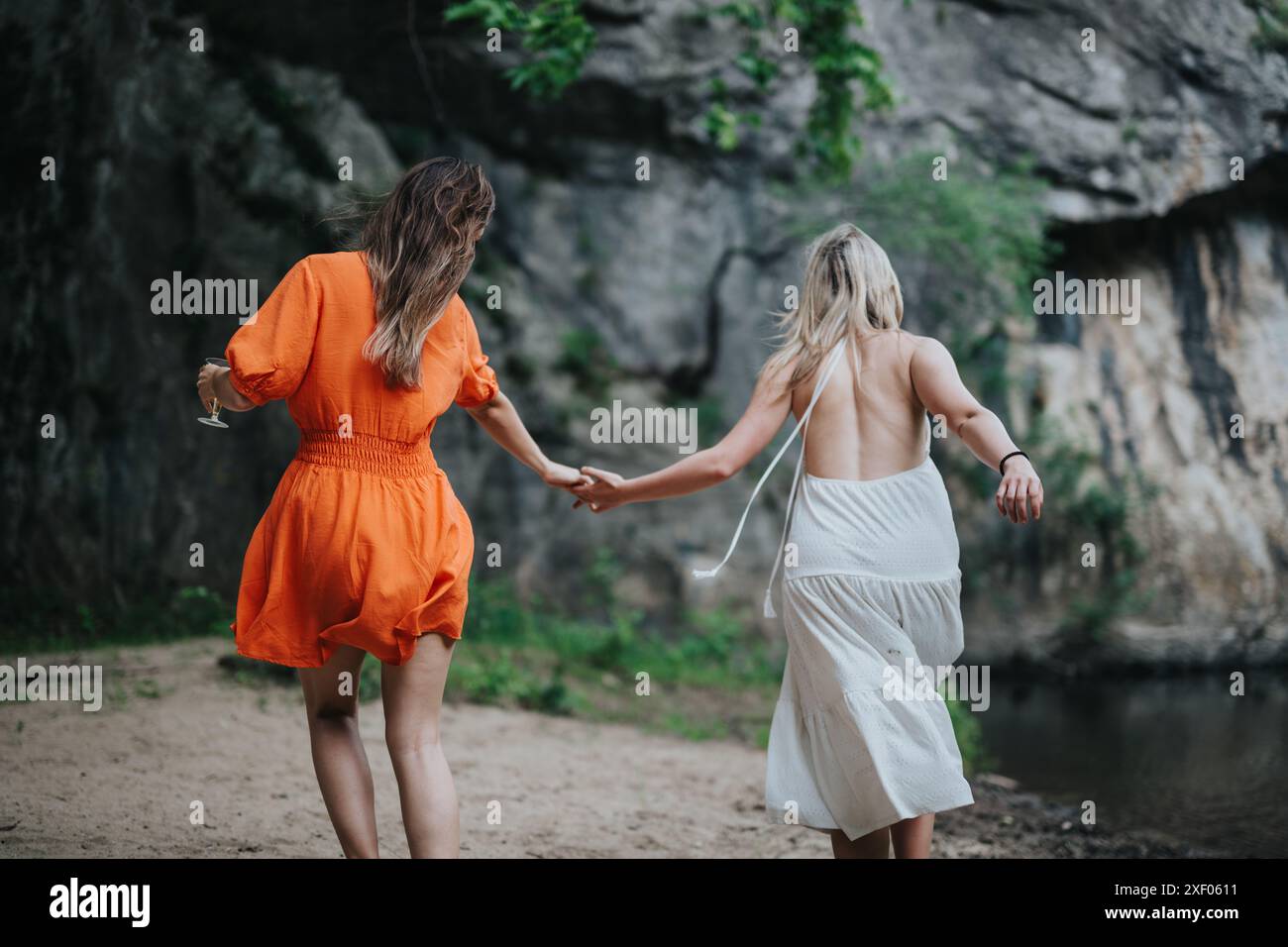 Two women holding hands while exploring nature in summer dresses Stock ...