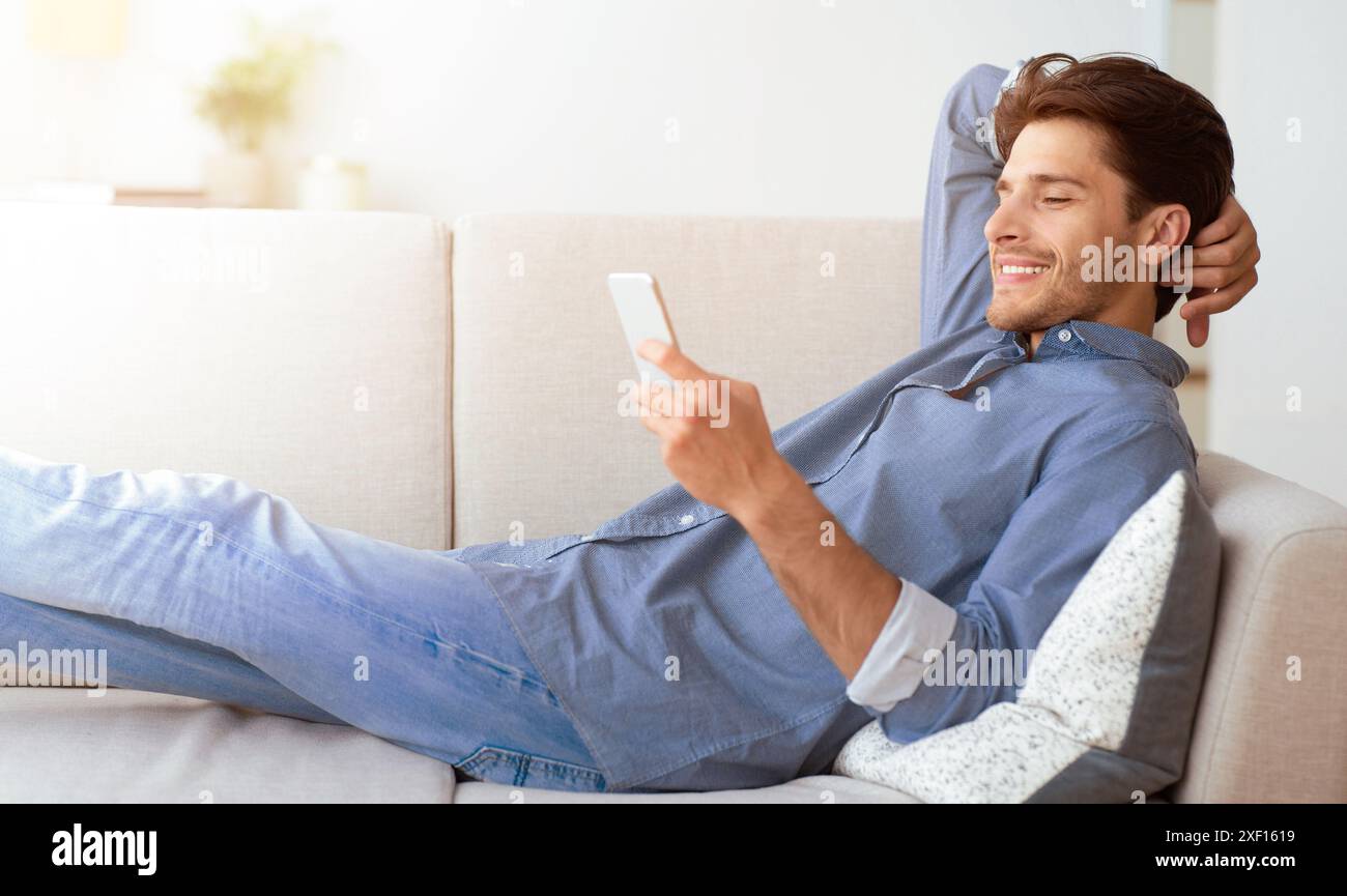 Man Relaxing on Couch Using Smartphone Stock Photo