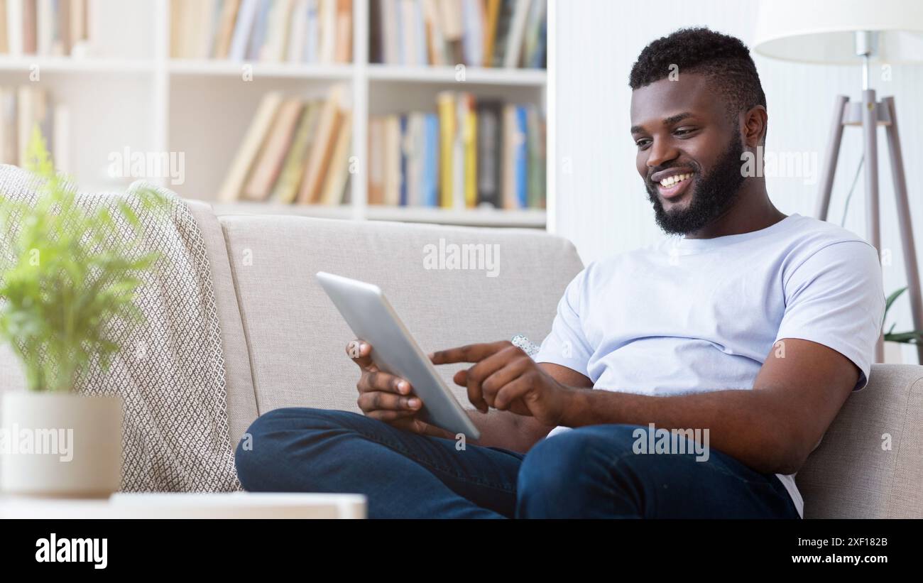 Happy Man Using Tablet While Relaxing on a Couch Stock Photo