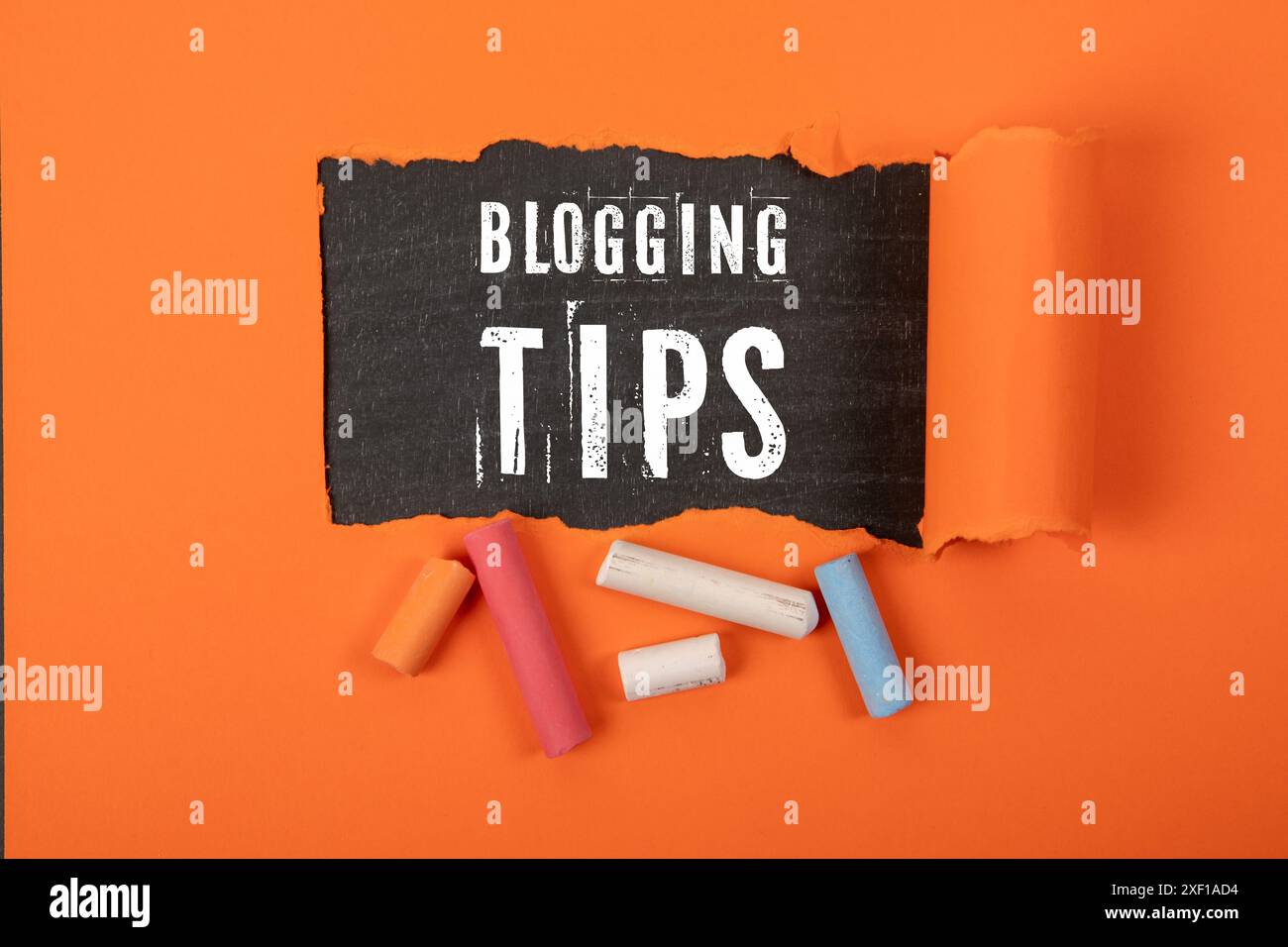 Blogging Tips. Text under torn orange paper on a blackboard. Stock Photo