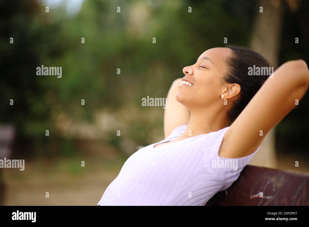 Profile of a happy black woman resting sitting on a bench in a park ...