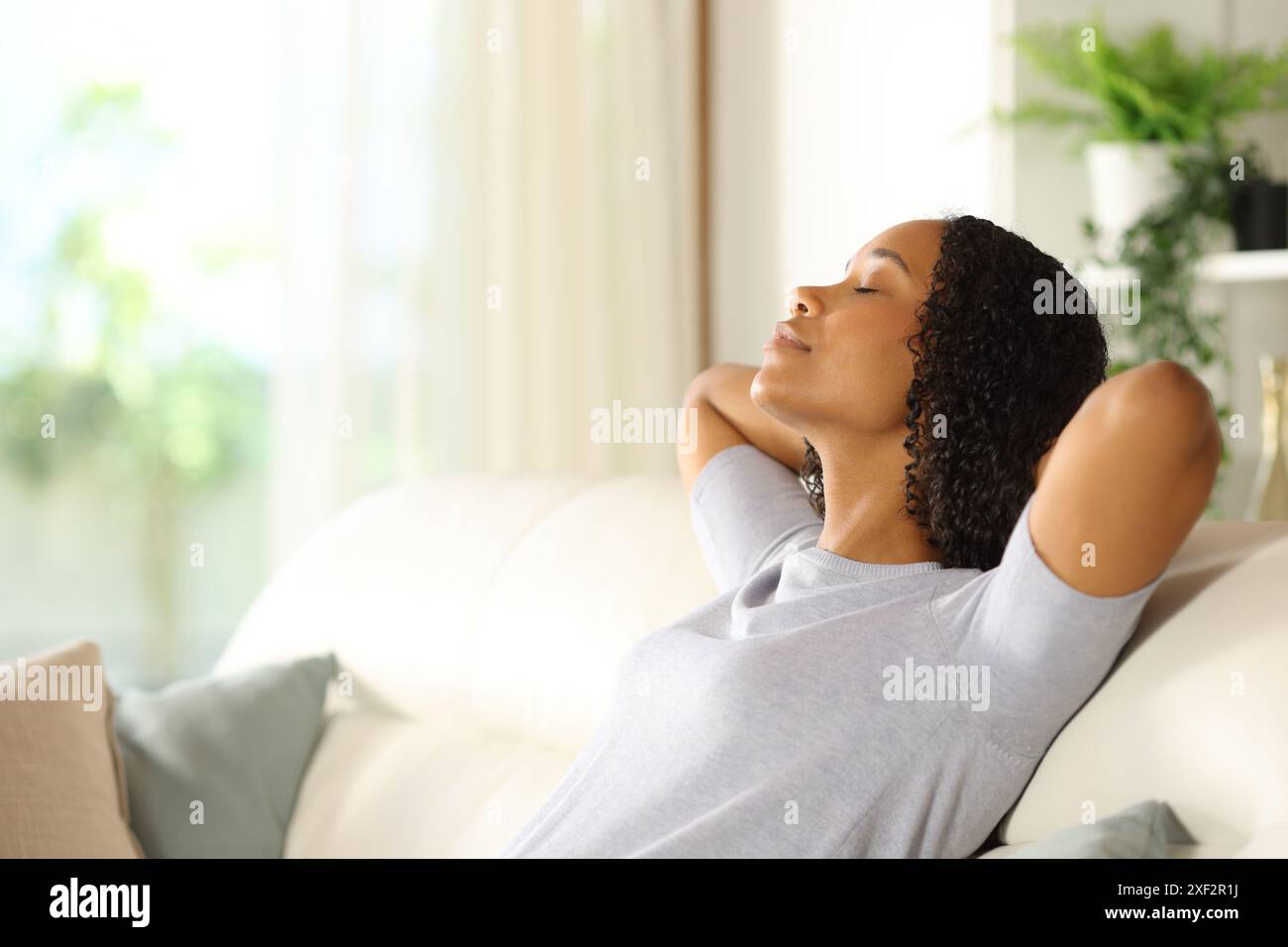 Profile of a black woman resting and relaxing sitting on a sofa at home ...