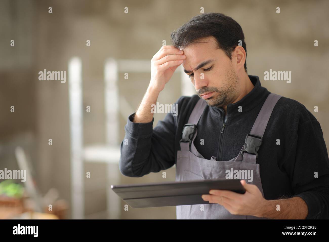 Worried construction worker checking tablet in a house Stock Photo
