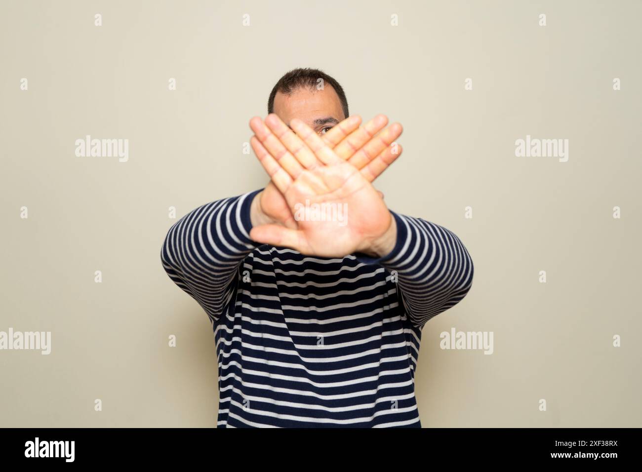 Hispanic man with beard standing over beige background rejection expression crossing arms and palms doing negative sign. Stock Photo